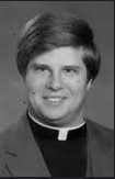 Black and white photo of Father Peter Burns smiling and wearing a Roman Catholic priest's collar.