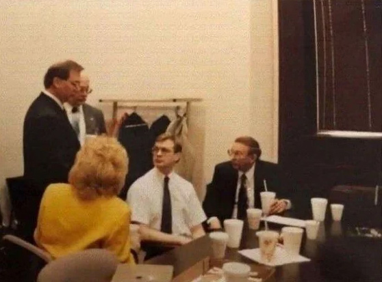 Jeffrey Dahmer seated with his father Lionel Dahmer, stepmother Shari Dahmer, and two unidentified men in a room with coffee cups on the table.