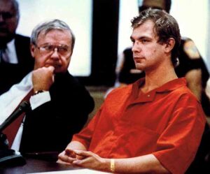 Photo of Jeffrey Dahmer, in an orange jail uniform, seated at the defense table between Gerald Boyle and Wendy Patrickus during a courtroom proceeding,