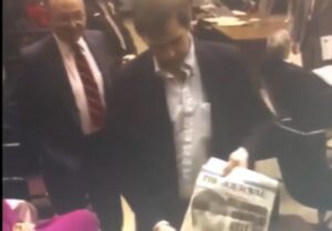 Still image from a video clip of Jeffrey Dahmer showing others in the courtroom a tabloid story about himself.