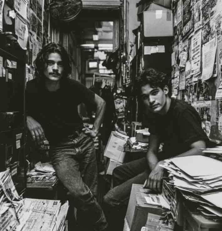 AI-generated illustration of two young office workers in a crowded adult-video business office surrounded by records, paperwork, and filing cabinets.