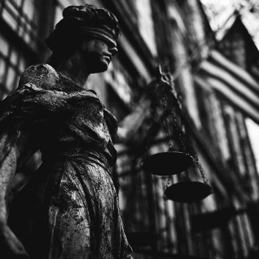 Black-and-white symbolic image of Lady Justice holding scales outside a courthouse.