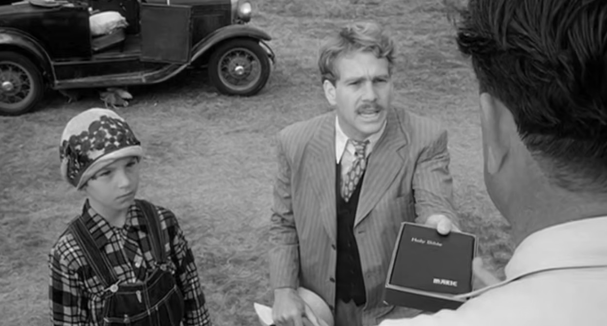 A traveling Bible salesman holds up a personalized Bible while a young girl watches in a black-and-white scene from Paper Moon.
